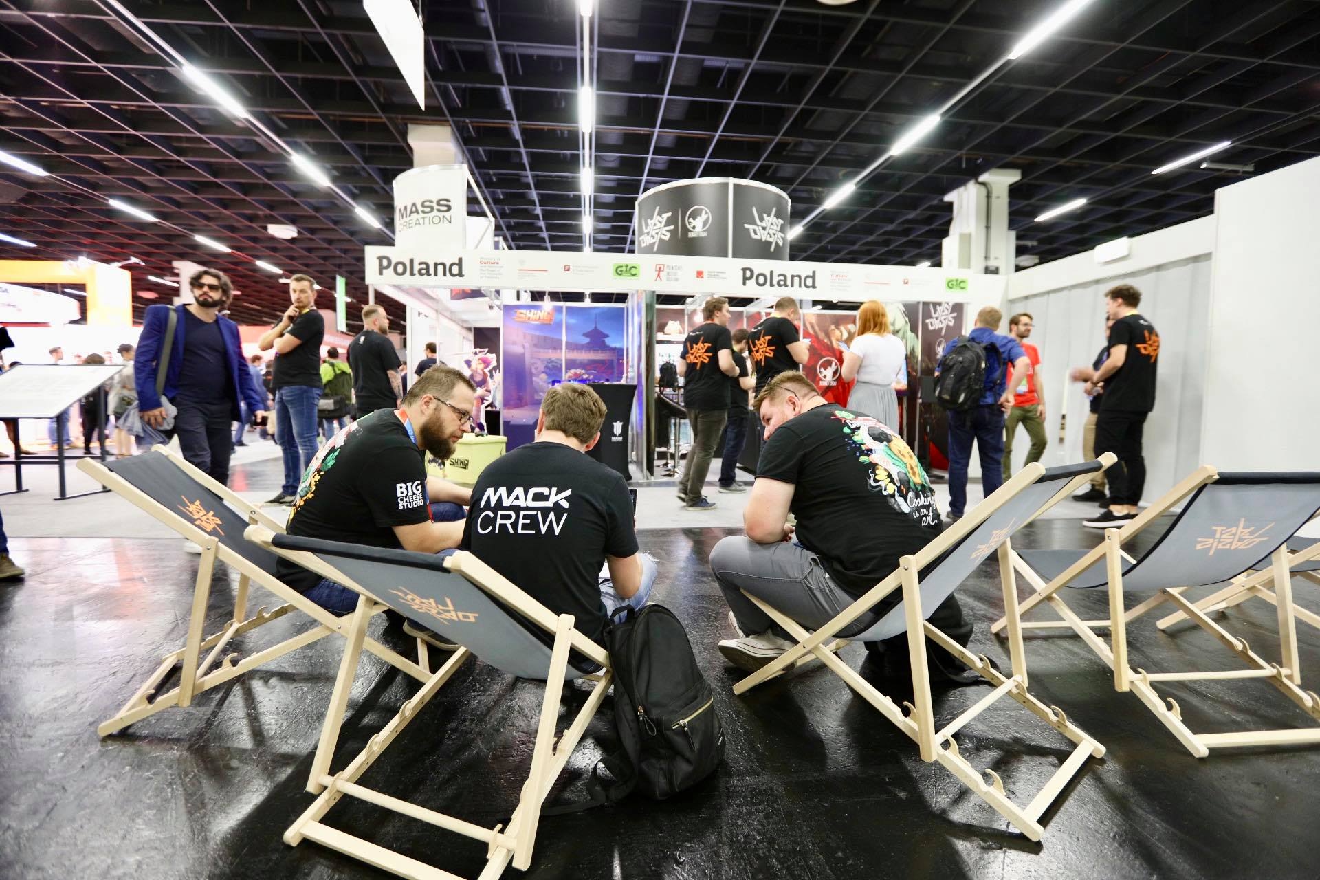 Trzy osoby siedzące na rozłożonych leżakach. W tle widać stoisko z napisem Poland